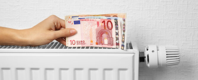 Eine Hand hält Geldscheine über einen Heizkörper.