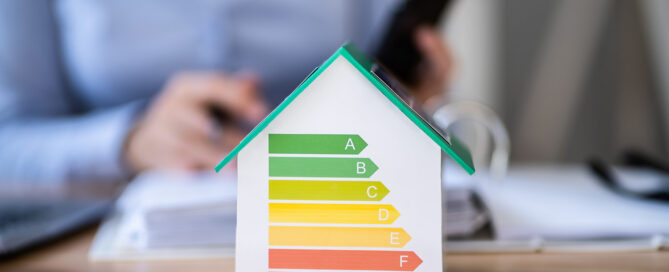 Miniaturhaus als Modell mit Energiebalken steht auf einem Schreibtisch.